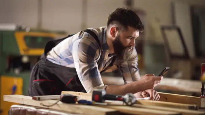 Ein Handwerker schaut auf sein Smartphone.