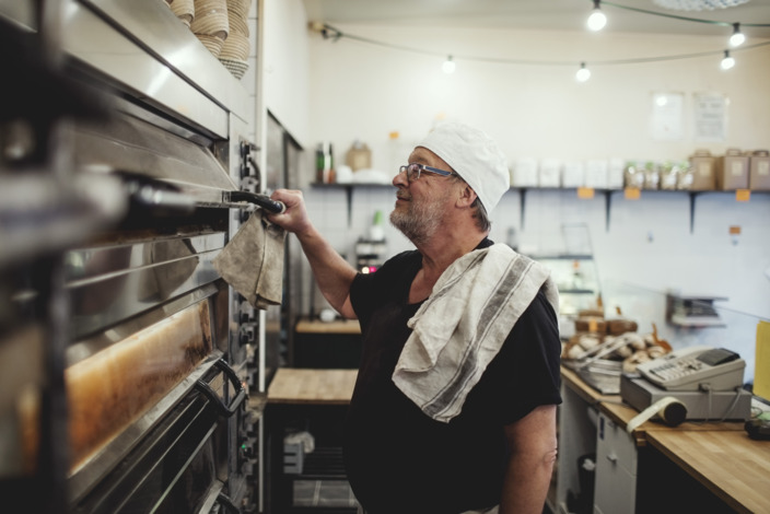 Ein Mann steht in einer Bäckerei und öffnet einen Ofen. 