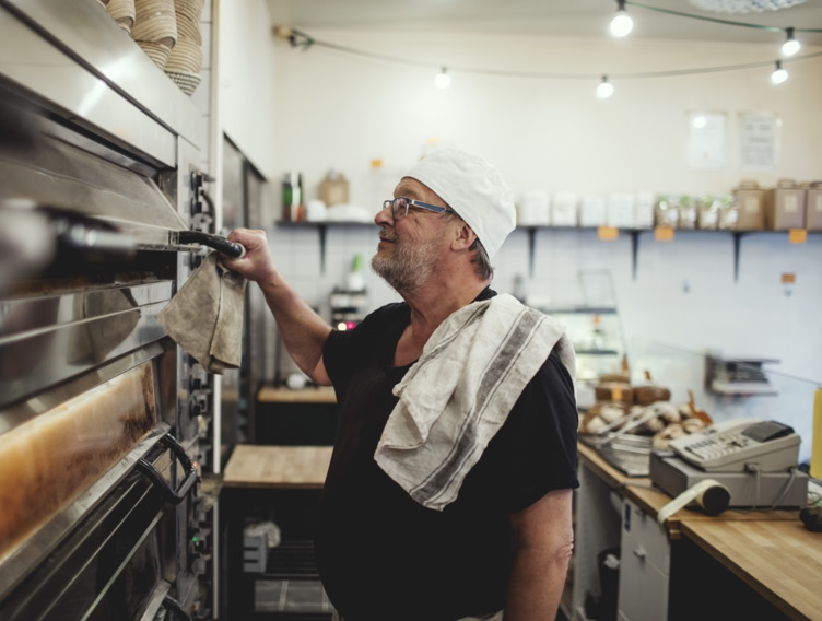 Ein Mann steht in einer Bäckerei und öffnet einen Ofen.