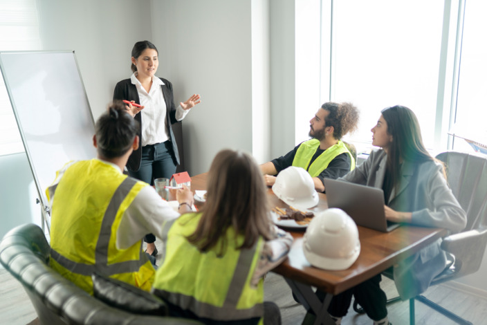 Junge Frau leitet Workshop in einem Büro mit Mitarbeitenden.