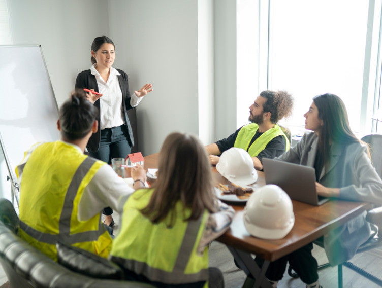 Junge Frau leitet Workshop in einem Büro mit Mitarbeitenden.
