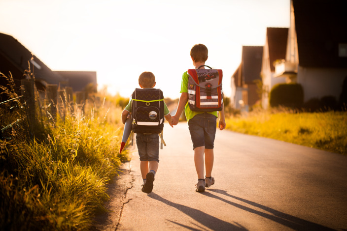Zwei Kinder mit Rucksäcken auf dem Weg zur Schule