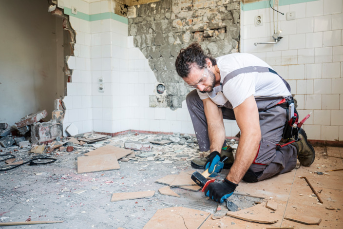 Handwerker steht gebückt auf einer Baustelle und macht Arbeiten am Boden