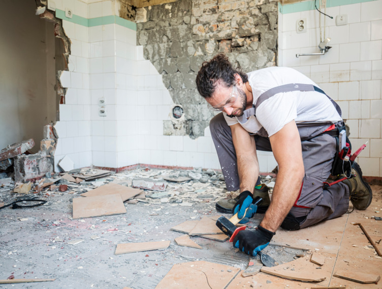 Handwerker steht gebückt auf einer Baustelle und macht Arbeiten am Boden