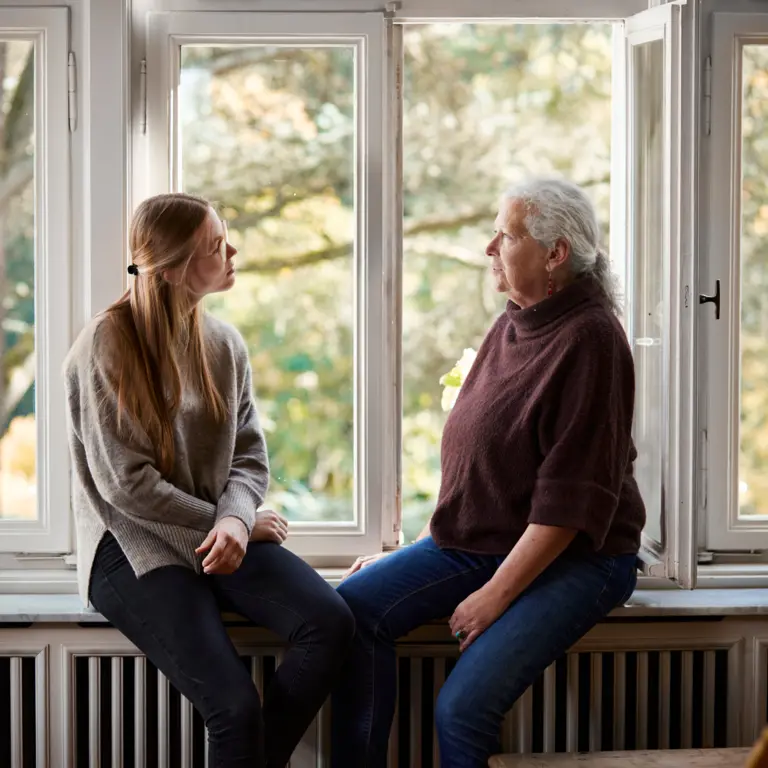 Zwei Frauen sitzen am Fenster auf einer Fensterbank und unterhalten sich