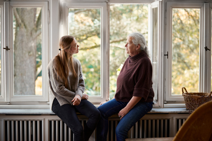 Zwei Frauen sitzen am Fenster auf einer Fensterbank und unterhalten sich