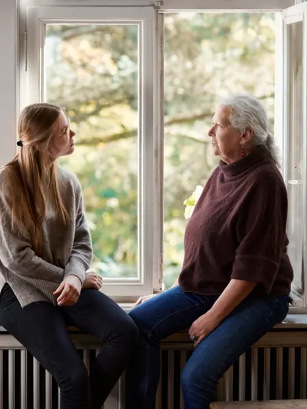 Zwei Frauen sitzen am Fenster auf einer Fensterbank und unterhalten sich