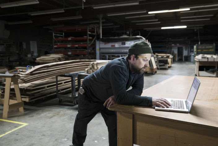 Handwerker steht an einem Tisch und sieht in seinen Laptop.