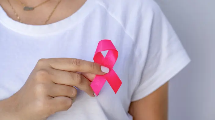 Frau hält eine rosa Schleife, welches als Symbol für Brustkrebs gilt