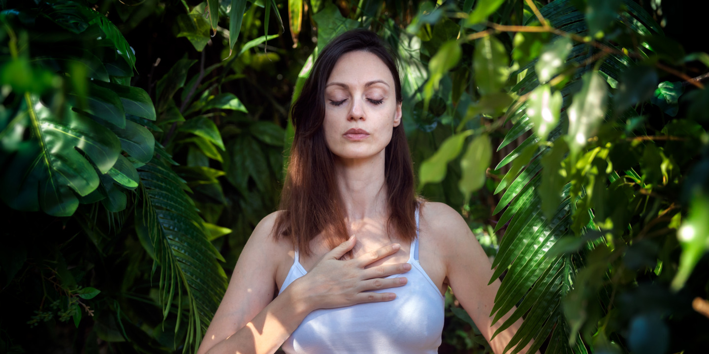 Junge Frau atmet mitten in der Natur durch und hält sich die Hand aufs Herz