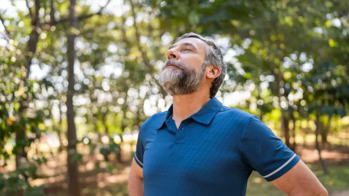 Mann im blauen T-Shirt atmet mit geschlossenen Augen durch 
