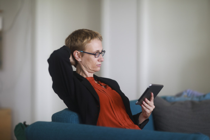 Eine Frau sitzt auf der Couch und schaut in ihr Tablet