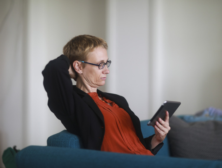 Frau lehnt sich auf dem Sofa zurück und schaut auf ihr Smartphone