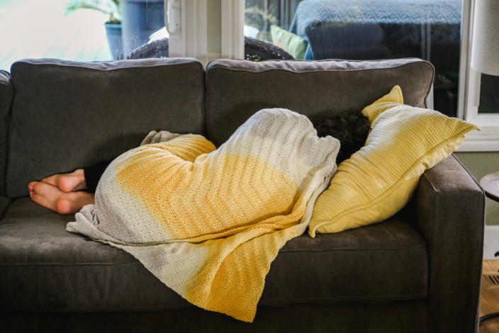 Frau liegt unter einer gelben Decke erkältet auf einer Couch 