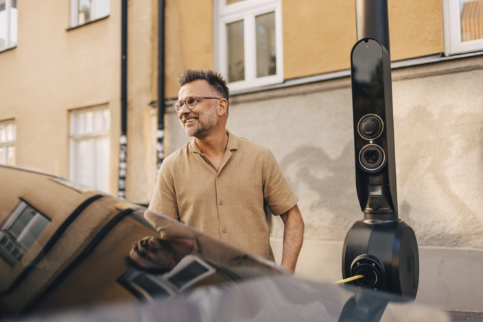 Mann lächelt, während er sein E-Auto lädt. 
