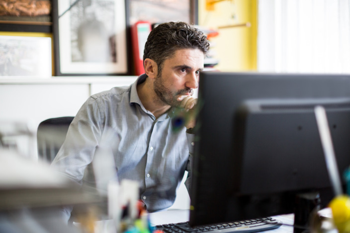 Mann sitzt im Büro und schaut in seinen Monitor. 