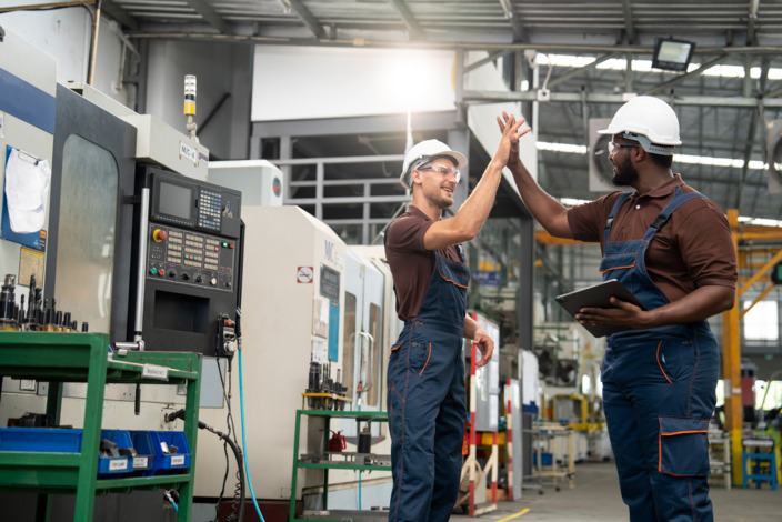 Zwei Handwerker geben sich ein High-Five in einer Werkstatt. 