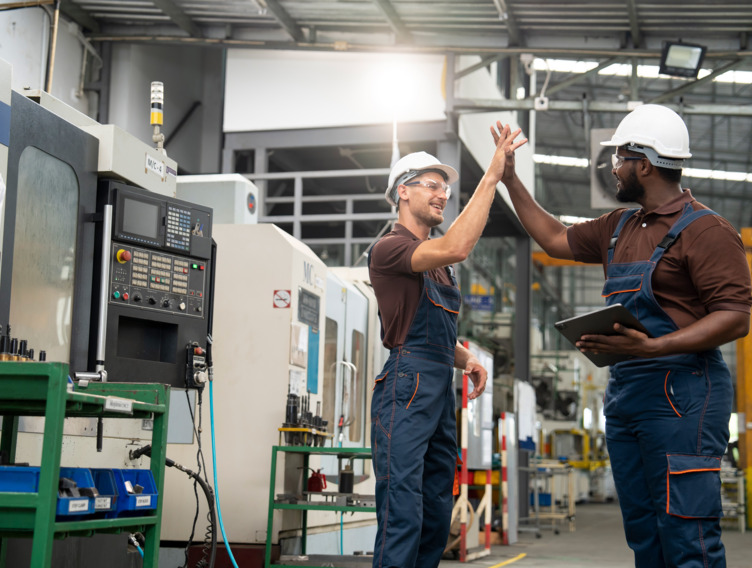 Zwei Handwerker stehen in einer Werkstatt und geben sich ein High-Five. 