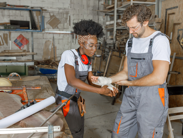 Eine Handwerkerin legt einem Mann einen Handverband an