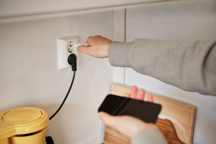 Eine Person steckt sein Smartphone-Ladekabel in eine Steckdose.
