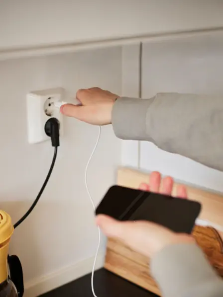 Eine Person steckt sein Smartphone-Ladekabel in eine Steckdose.
