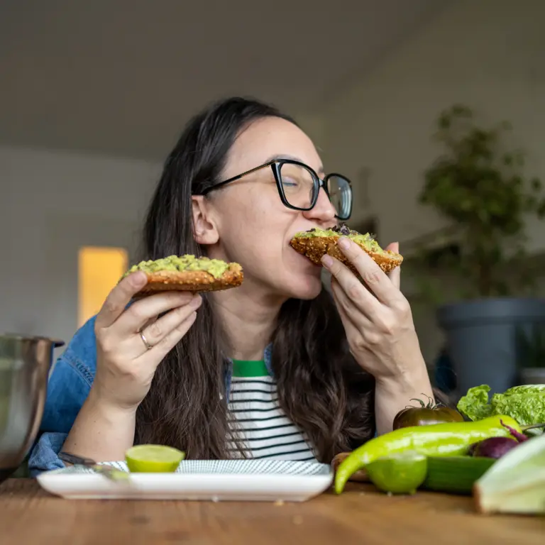 Frau beißt in ein Brot, das mit Avocado bestrichen wurde