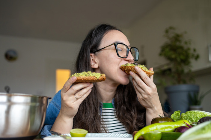 Frau beißt in ein Brot, das mit Avocado bestrichen wurde