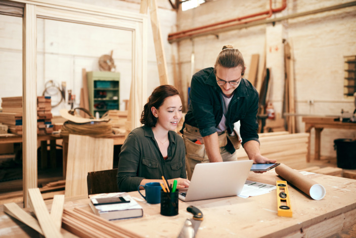 Eine Handwerkerin und ein Handwerker sitzen gemeinsam vor dem Laptop.