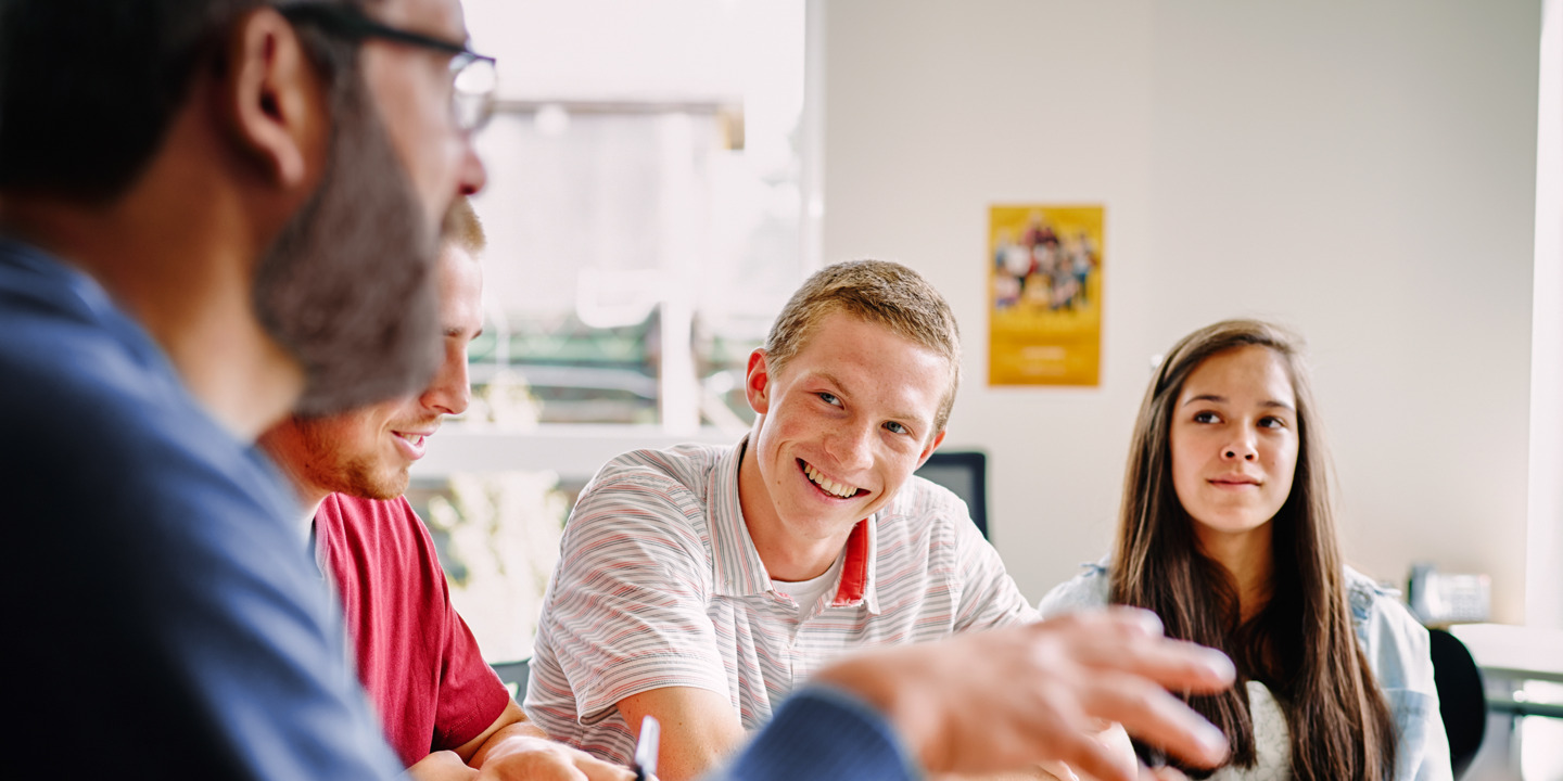 Lehrer sitzt mit Schülern am Tisch in einer angeregten Diskussion