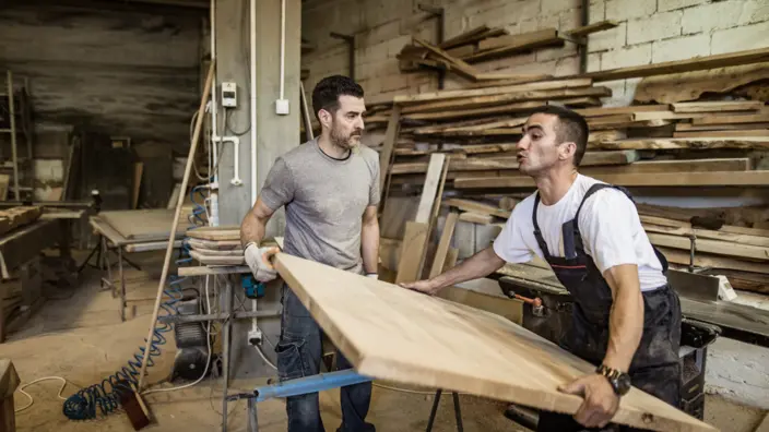 Zwei Handwerker heben eine große Holzplatte.