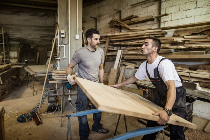 Zwei Männer heben eine große Tischplatte in der Werkstatt