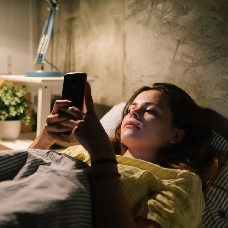 Frau liegt im Bett und schaut auf ihr Smarthone. 