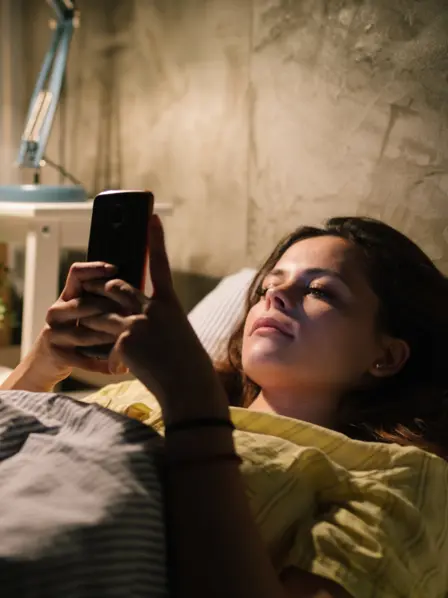 Frau liegt im Bett und schaut auf ihr Smarthone. 