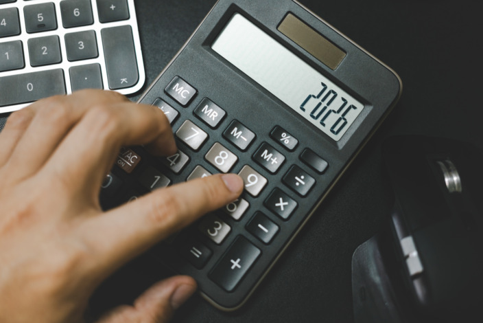 Eine hand tippt die Zahl 2026 in einen Taschenrecher. 