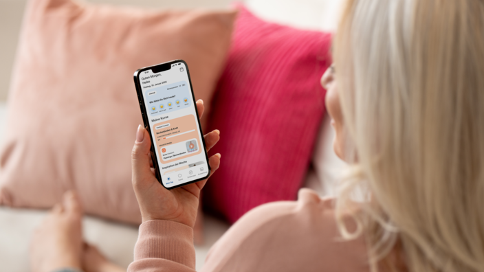 Frau sitzt auf ihrem Sofa und schaut sich auf ihrem Smartphone die femfeel App an.