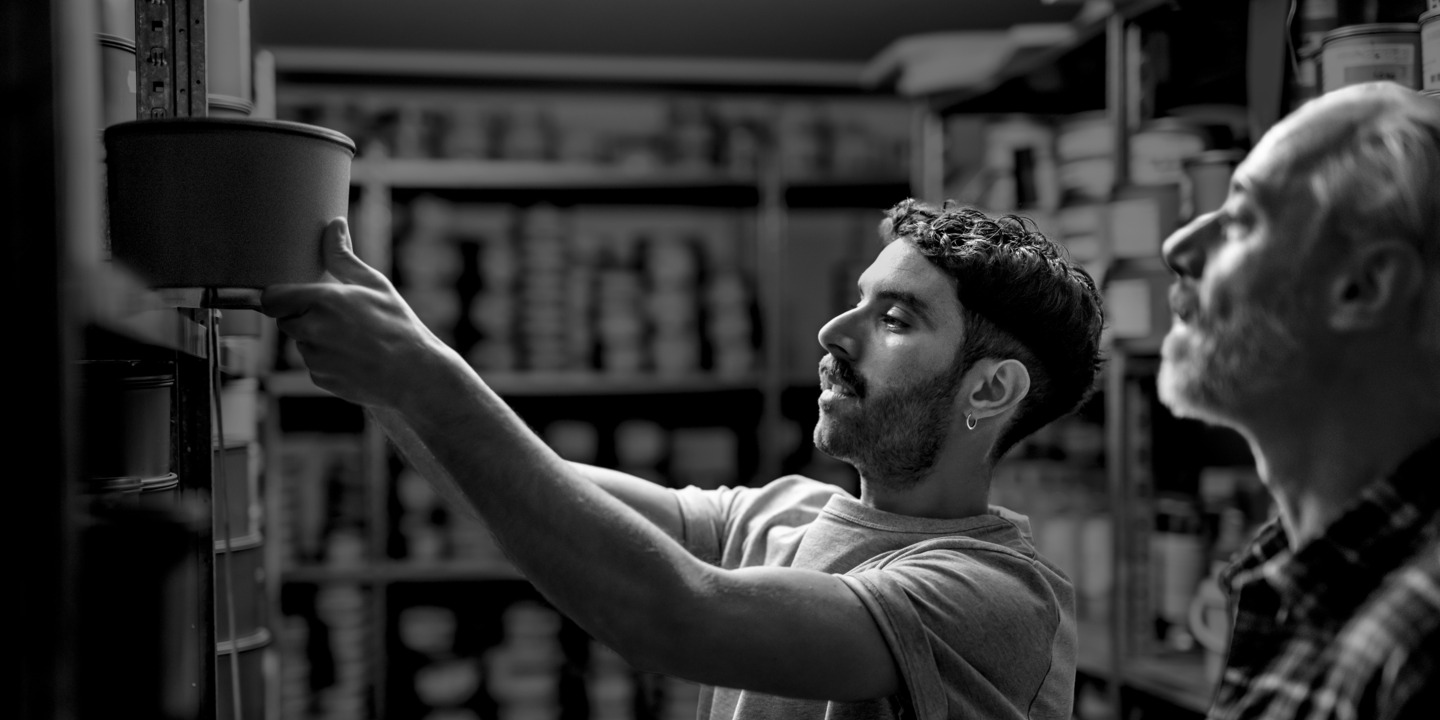 Zwei Männer in einer Druckerei stehen vor einem Regal. 