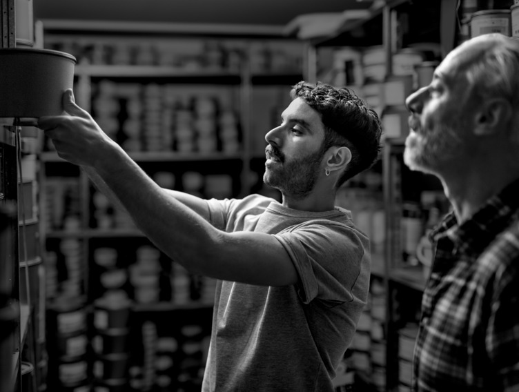 Zwei Männer in einer Druckerei stehen vor einem Regal. 