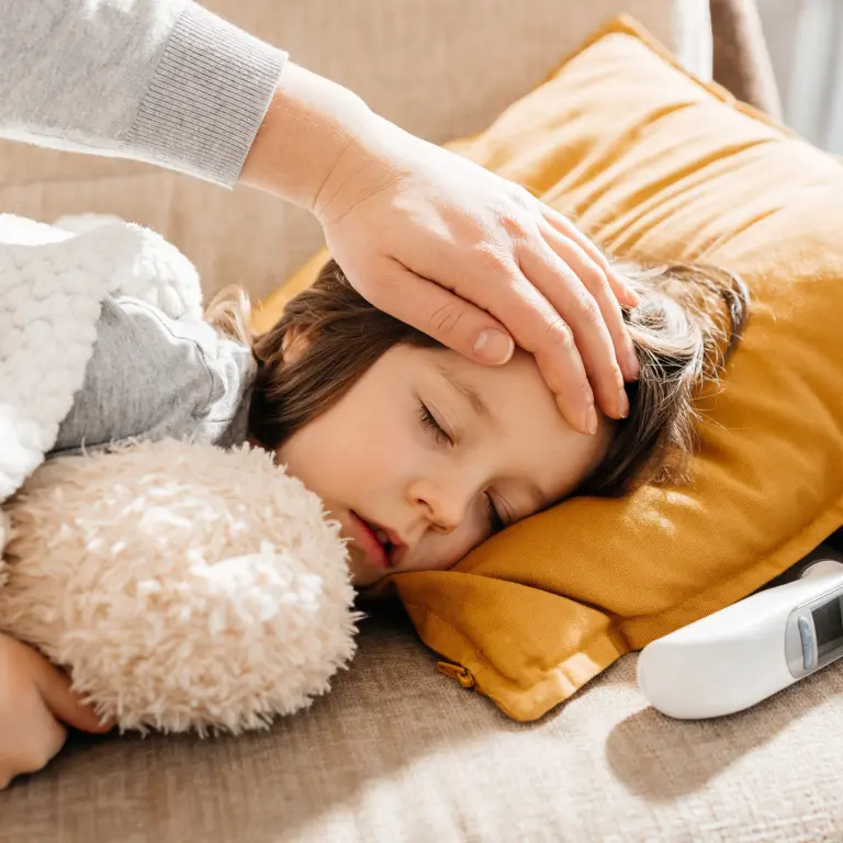 Ein krankes Kind liegt auf der Couch neben einem Fieberthermometer.