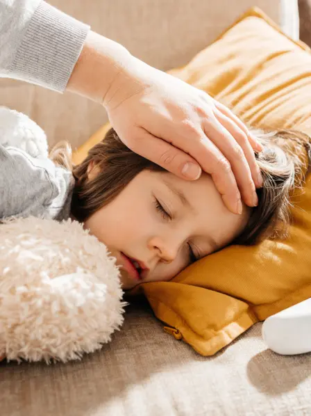 Ein krankes Kind liegt auf der Couch neben einem Fieberthermometer.