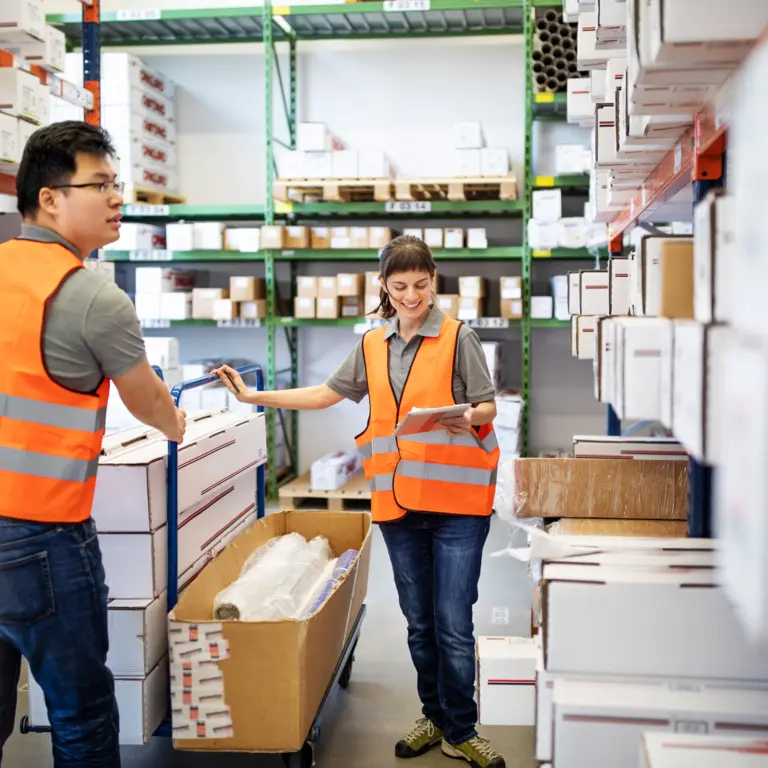 Eine Handwerkerin und ein Handwerker stehen in einem Lager.