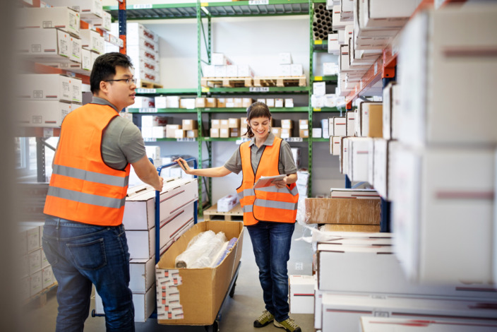 Eine Handwerkerin und ein Handwerker stehen in einem Lager.