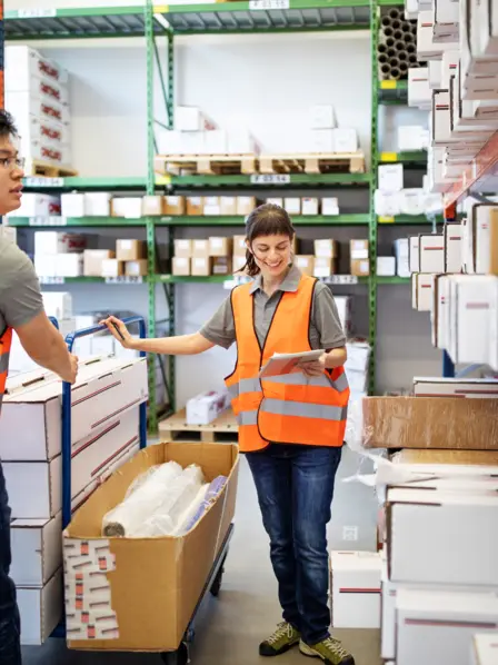 Eine Handwerkerin und ein Handwerker stehen in einem Lager.