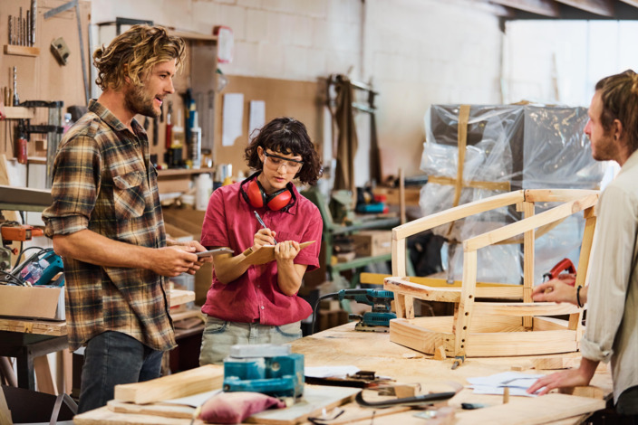 Ein Team von Handwerkern steht in einer Werkstatt und berät sich. 