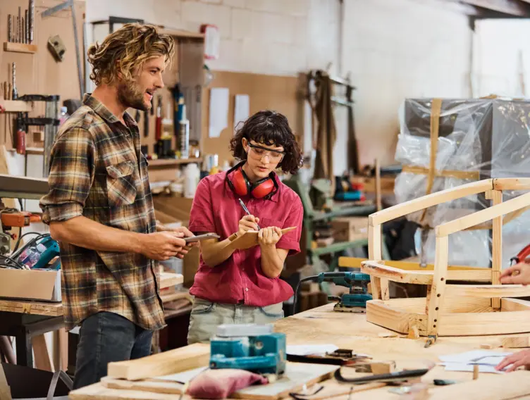 Handwerkende stehen in einer Tischlerei an einem Arbeitstisch.