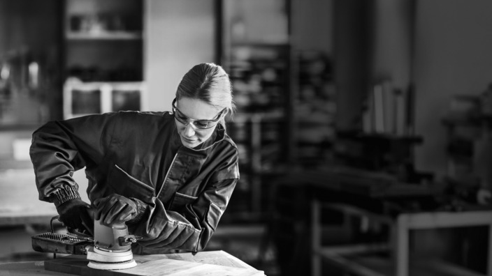 Junge Frau arbeitet in der Werkstatt mit Sicherheitsbrille
