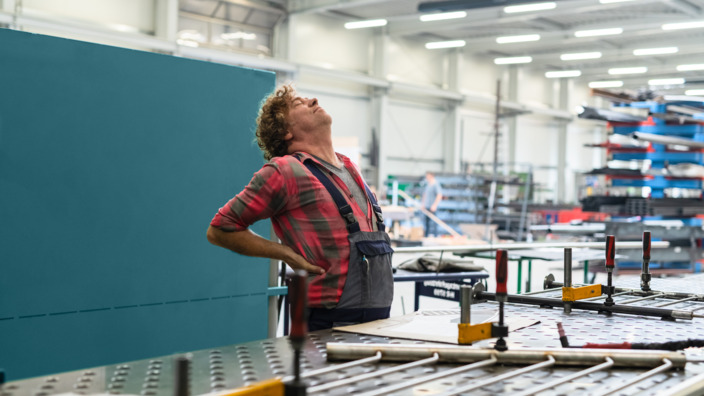 Metallbauer steht in der Werkstatt und hält sich den Rücken