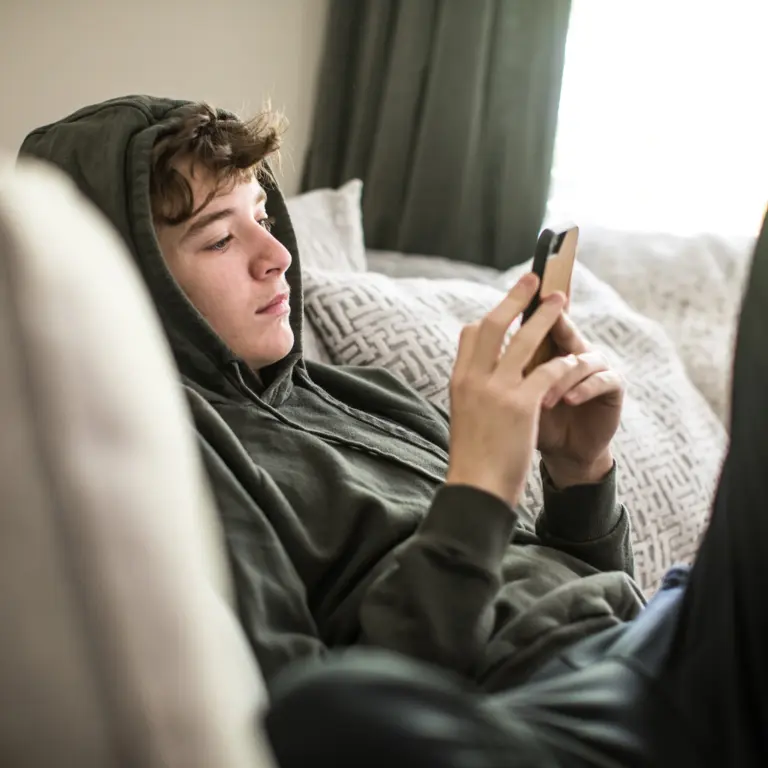 Jugendlicher sitzt auf dem Sofa und schaut auf sein Smartphone. 
