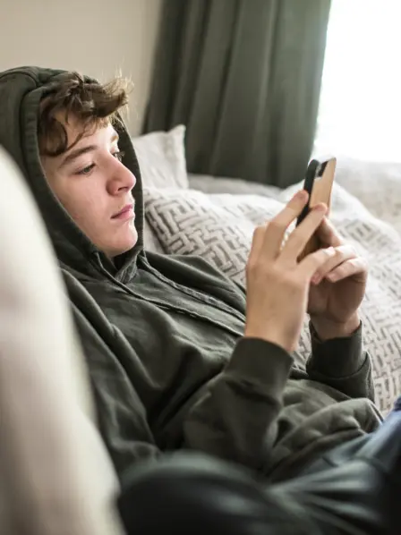 Jugendlicher sitzt auf dem Sofa und schaut auf sein Smartphone. 