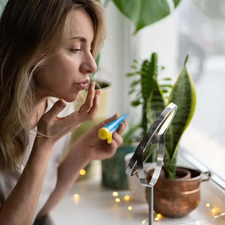 Frau behandelt ihren Lippenherpes vor einem Spiegel. 