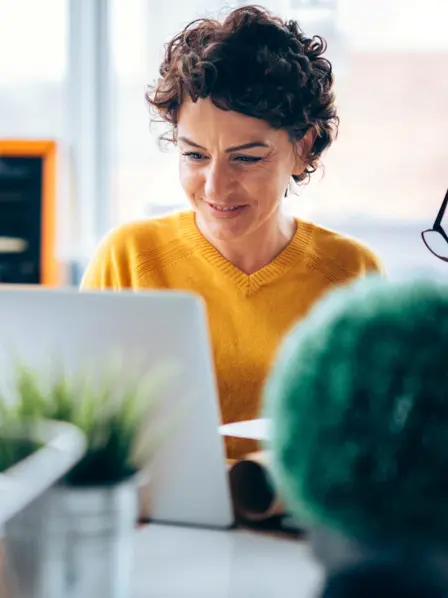 Frau im gelben Pulli sitzt vor ihrem Laptop.